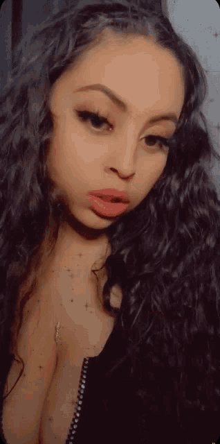 a woman with long black hair is wearing a black top and a necklace .