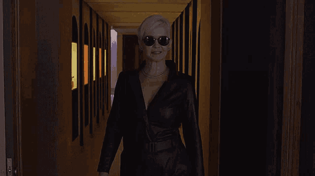 a woman wearing sunglasses and a black leather jacket stands in a hallway