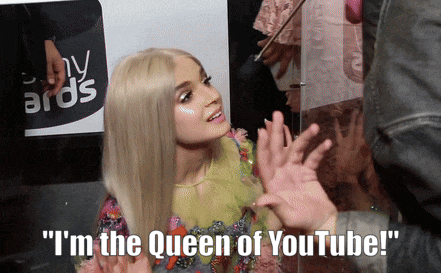 a woman says " i 'm the queen of youtube " in front of a sign that says awards