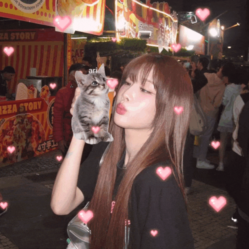 a girl holding a kitten in front of a pizza story stand
