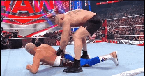 two men are wrestling in a wrestling ring and one of them is laying on the ground .