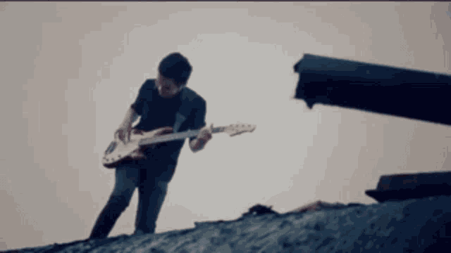 a man playing a guitar on top of a rock
