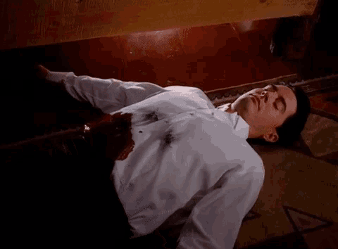 a man in a white shirt is laying on the floor with blood coming out of his shirt .