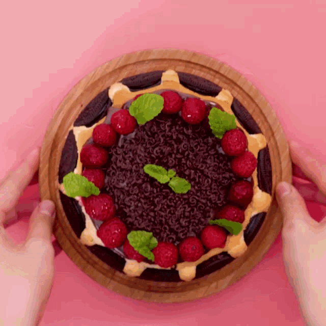 a person is holding a pizza with raspberries and mint leaves on it