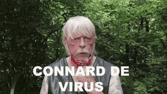 a man with a bandana around his neck is standing in front of trees and says " connard de virus "
