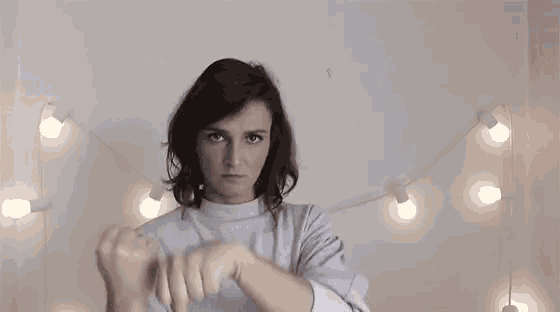 a woman in a grey sweater is giving the middle finger to the camera