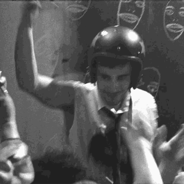 a man wearing a helmet stands in front of a blackboard with faces drawn on it