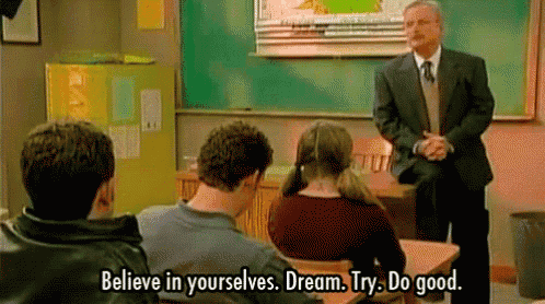 a man in a suit and tie is standing in front of a group of students in a classroom and talking to them .