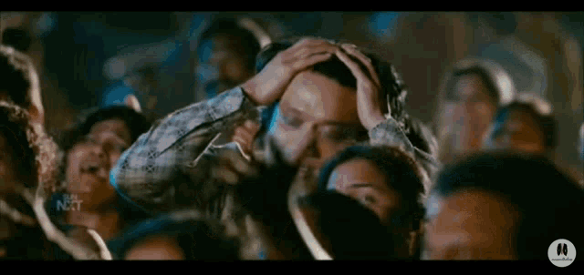 a man is holding his head in his hands in a crowd of people at a concert .