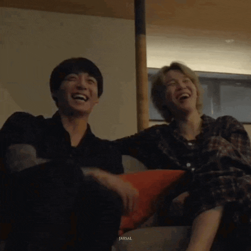 a couple of men are sitting on a couch laughing .