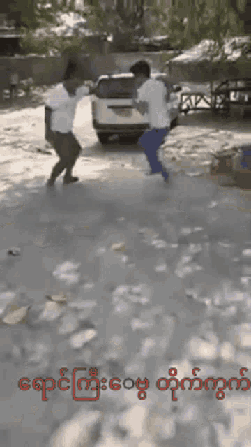 two men are dancing in front of a car in a parking lot with foreign writing