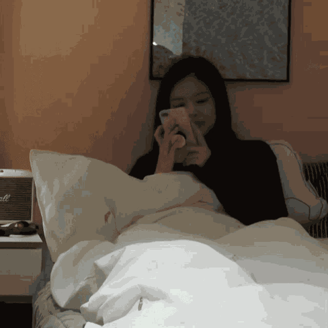 a woman is laying on a bed looking at her phone next to a marshall speaker