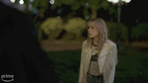 a woman wearing a white fringed jacket is screaming in front of an amazon prime logo