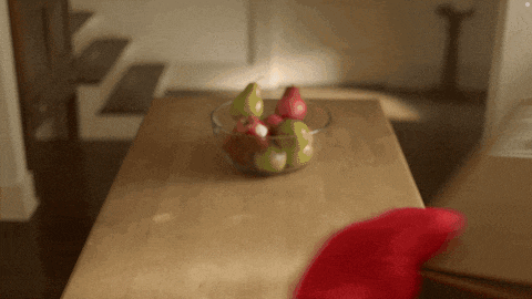 a bowl of fruit on a wooden table with a red hat in the foreground