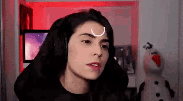 a woman wearing headphones with a crescent moon on her forehead is sitting in front of a snowman .