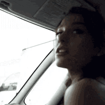 a woman is sitting in a car looking out the window .