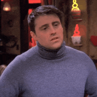 a man wearing a turtleneck sweater is standing in front of a shelf with a heart on it .