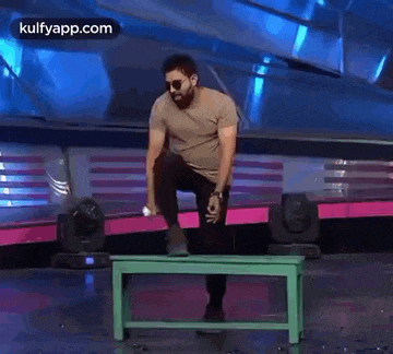 a man with a beard is standing on a green bench on a stage .