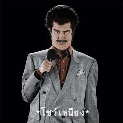 a man in a suit and mustache is holding a microphone and speaking into it .