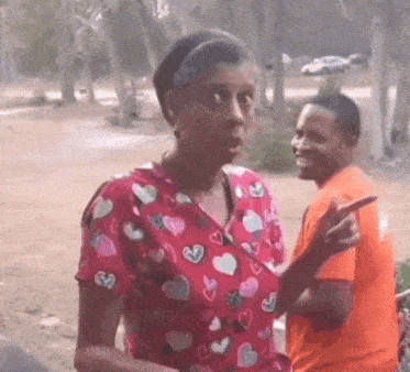 a woman wearing a pink scrub top with hearts on it is standing next to a man in an orange shirt .