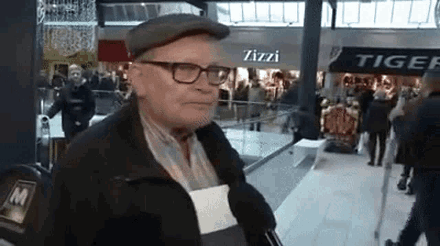 an older man wearing glasses and a hat is standing in front of a store called zizzi