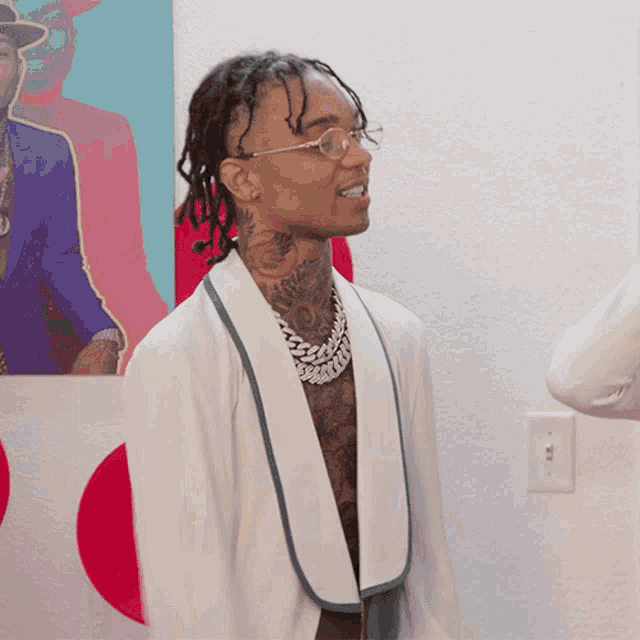 a man wearing glasses and a white jacket stands in front of a painting