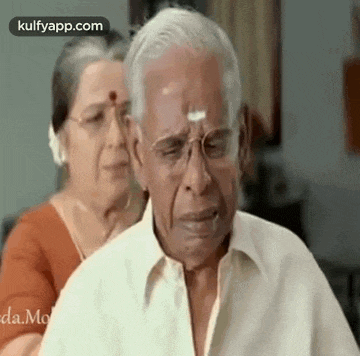 an elderly man with glasses is crying while a woman holds his shoulders .