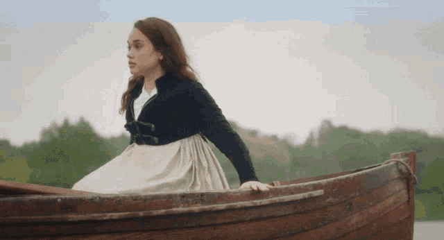 a woman in a black jacket sits in a boat on a lake