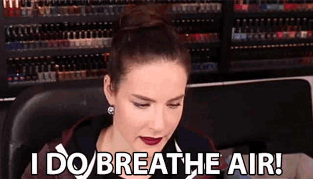 a woman is sitting in front of a wall of nail polish and says `` i do breathe air ! ''
