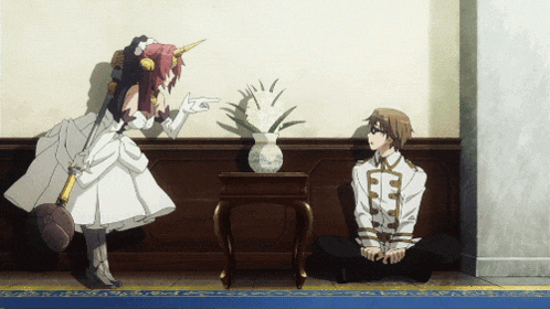 a man sits on the floor while a woman points at a pineapple on a table