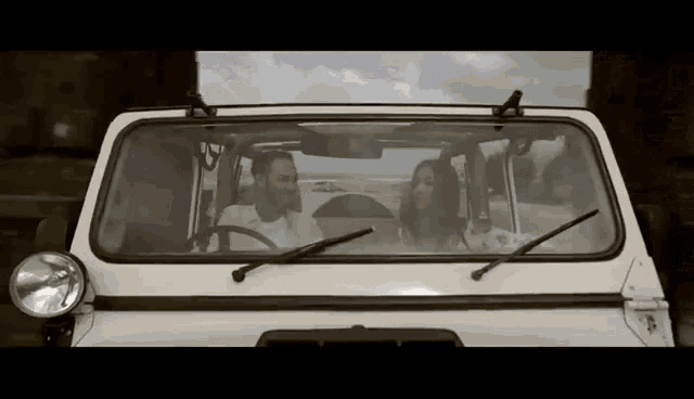 a man and woman are sitting in a car looking out the windshield