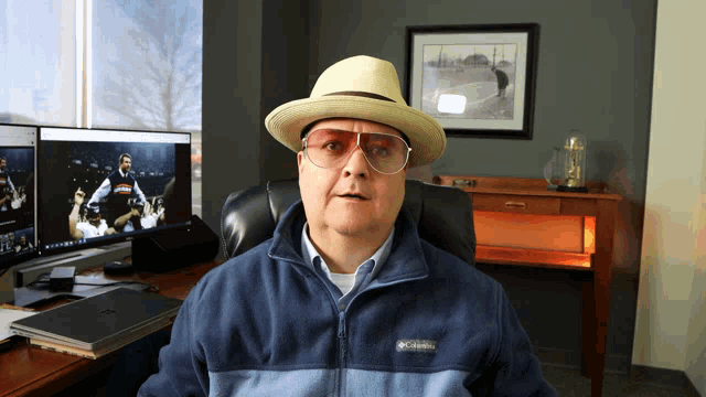 a man wearing a hat and glasses sits in front of a columbia jacket