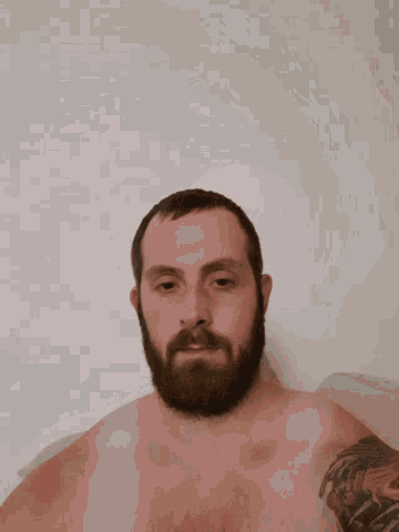 a shirtless man with a beard and a tattoo on his arm is taking a bath