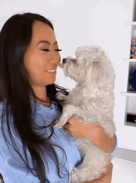 a woman is holding a small white dog and the dog is sniffing the woman 's nose