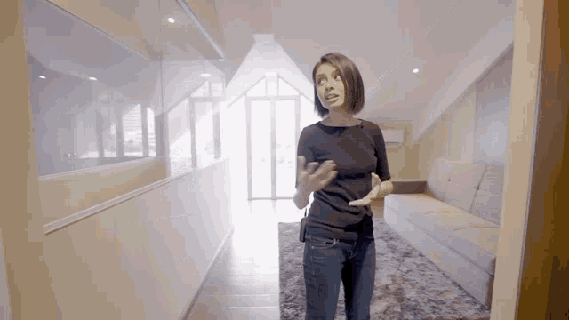 a woman in a black shirt is standing in a hallway with a couch