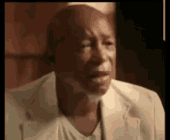 a bald man with a beard is crying while wearing a white suit and a white shirt .