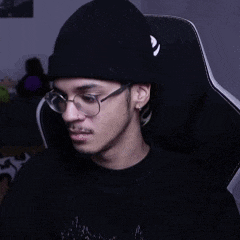 a young man wearing glasses and a black beanie is sitting in a chair