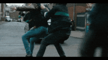 a man in a black jacket is kicking another man in a street