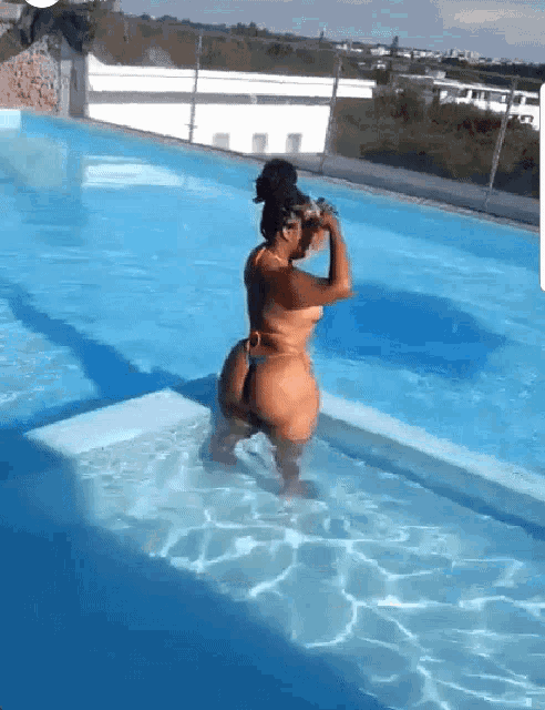a woman in a bikini is standing in a swimming pool drinking water