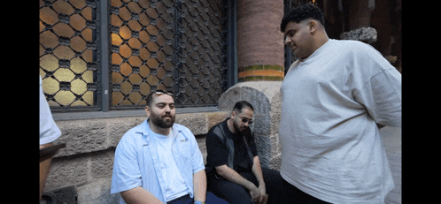 a man with a beard sits on a bench talking to two other men