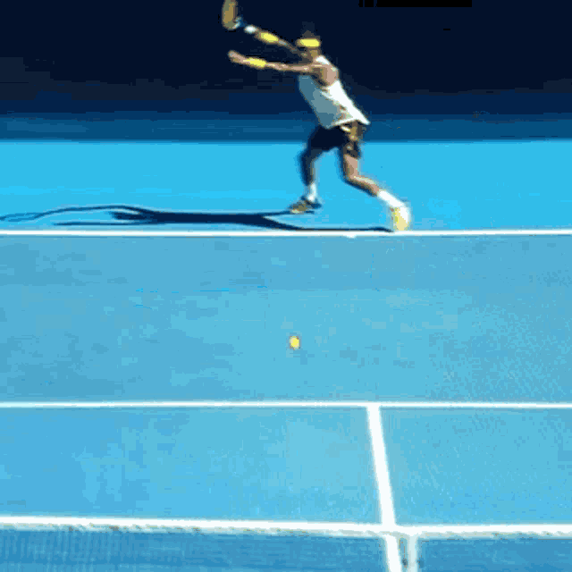 a tennis player swings a racket at a yellow ball on a blue court