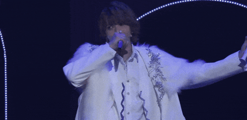 a man in a white jacket is singing into a microphone on a stage