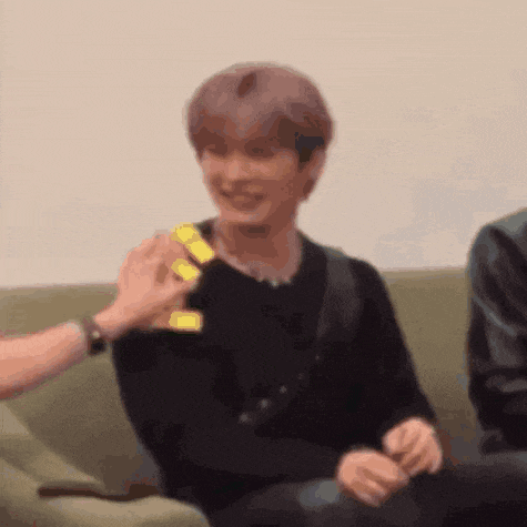 a man is sitting on a couch with a person holding a yellow object in front of him .