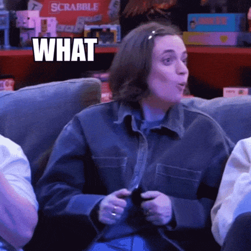 a woman sitting on a couch playing a video game with the word what above her head
