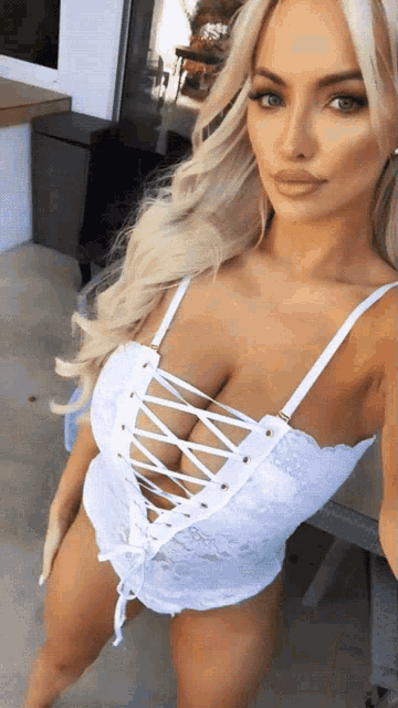 a woman in a white lace up top is taking a picture of herself
