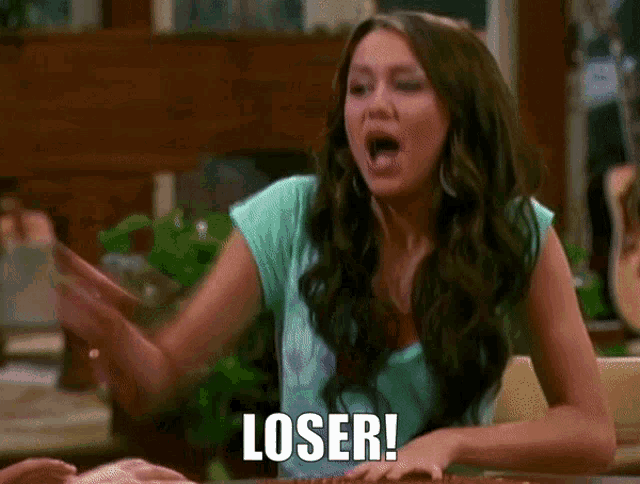 a woman in a blue shirt is saying loser with her hands in the air