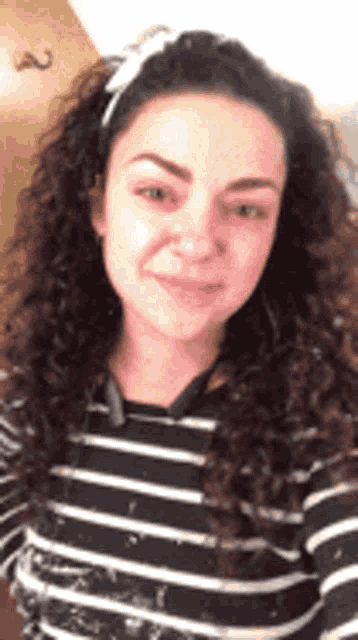 a woman with curly hair is wearing a striped shirt and a headband and smiling .
