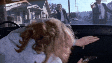 a man is pointing a gun at a woman in a car while another man looks on .