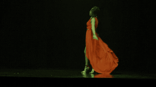 a woman in a long red dress is dancing in a dark room