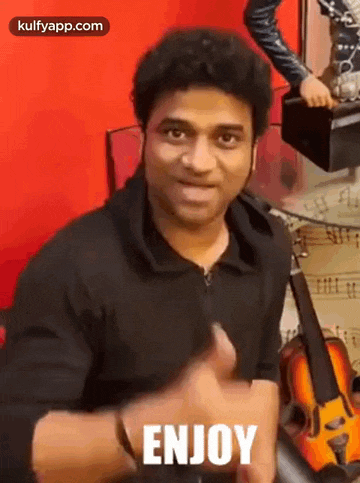 a man is giving a thumbs up in front of a violin and the word enjoy is on the screen .